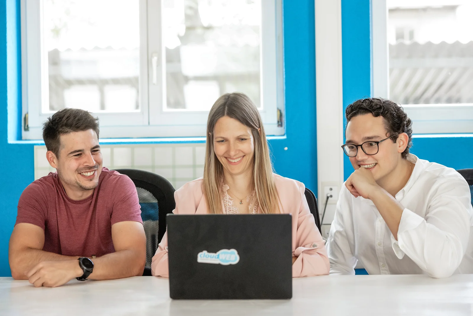 Drei Personen aus dem cloudWEB-Team schauen gemeinsam auf einen Laptop